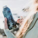 woman in white long sleeve shirt holding blue glass bottle