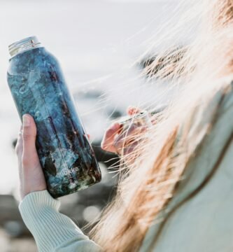 woman in white long sleeve shirt holding blue glass bottle